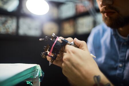 Young tattooist preparing tattoo-device for workの写真素材