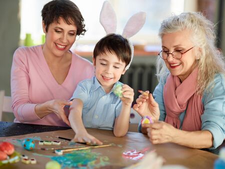 Two women and little boy painting eggs for Easterの写真素材