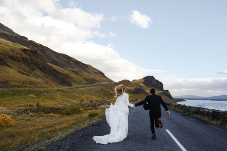 Newlyweds running down highway between river and mountainの写真素材
