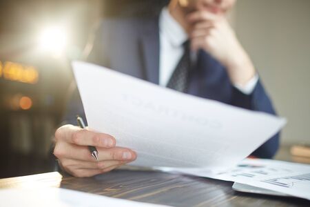 Closeup portrait of unrecognizable successful businessman wearing black formal suit analyzing documents and finance statistics at desk, thinkingの写真素材
