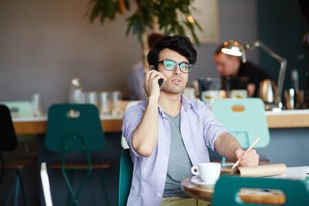 Young Man Speaking by Phone Working in Cafeの写真素材
