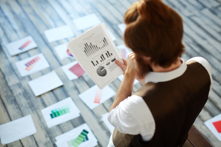 Pensive specialist looking at chart on paperの写真素材