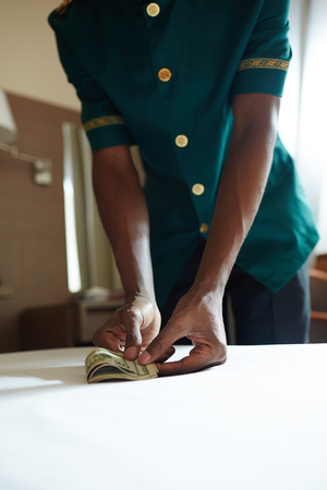Closeup shot of unrecognizable African bellhop taking cash money from table in hotel roomの写真素材
