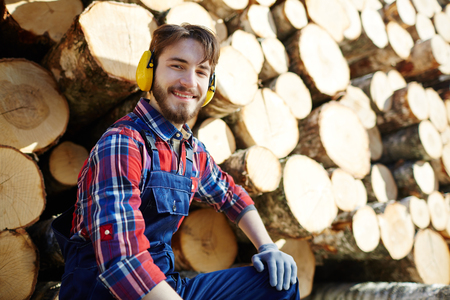 Smiling Lumberjack with Pile of Tree Trunks