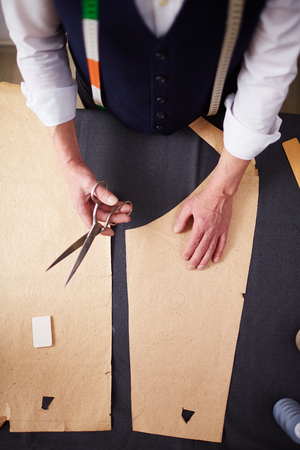Directly above shot of tailor  working in atelier studio, cutting suit patterns on fabric