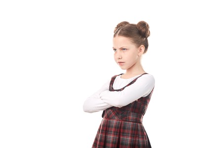 Portrait of offended girl in school uniform standing cross-armed against white background