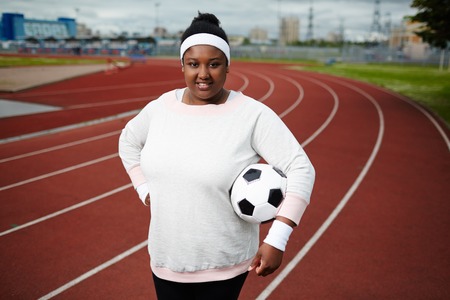 Plump woman posing with soccer ball at track and field stadiumの写真素材