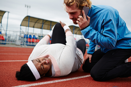 Plump woman lying on running track, her trainer calling emergency serviceの写真素材