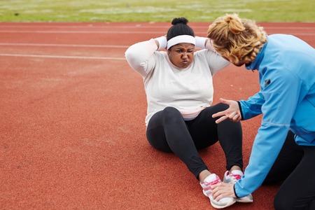 Plus-size African woman doing sit-ups exercise guided by personal trainer