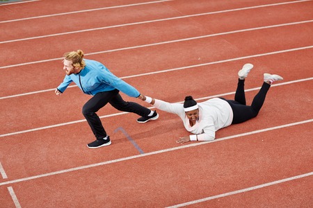 Determined personal trainer dragging exhausted overweight woman on trackの写真素材