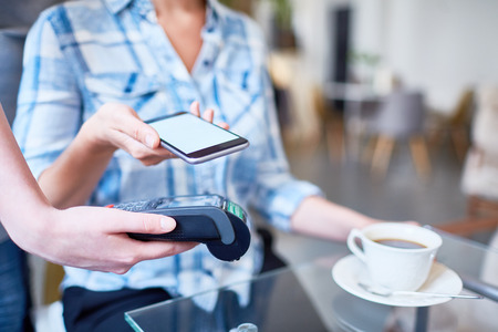 Close-up shot of unrecognizable woman using mobile phone in order to pay for her coffee at lovely...