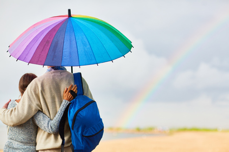 Back view of tourists with backpack standing under colorful umbrella in rural environmentの写真素材