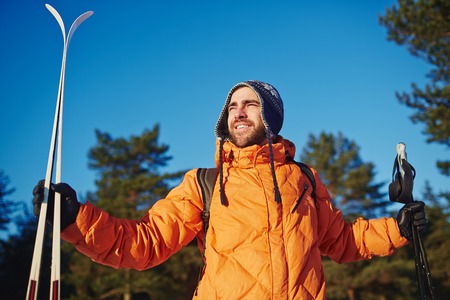 Young sportsman with skis looking around and admiring beauty of winter forest on sunny dayの写真素材