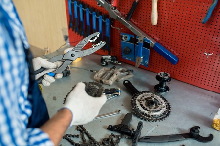 Gloved hands of master holding pliers and chain during bibycle repairの写真素材