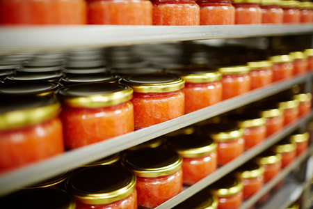 Salted red caviar in small jars standing on shelves in seafood producing plantの写真素材