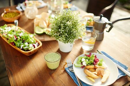 Glass of fresh vegetable smoothie, salad and roasted potatoes on plate, homemade lemonade and other food served on tableの写真素材