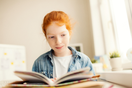 Clever little book lover sitting in library at leisure with open book in frontの写真素材