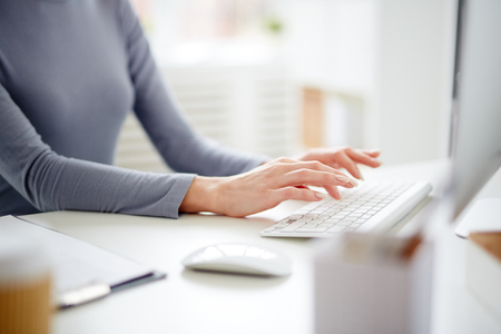Hands of young secretary over computer keyboard typing by workplaceの写真素材