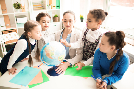 Cute pupils and teacher in the classroom with globe at the primary schoolの写真素材