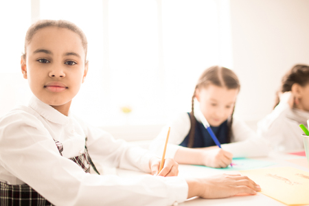 Portrait of African schoolgirl sitting at desk and writingの写真素材