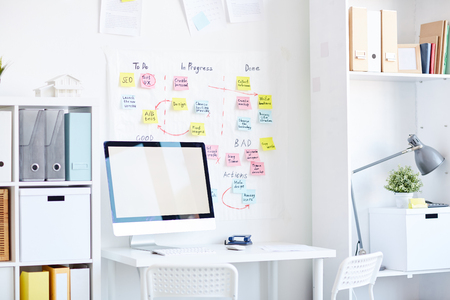 Modern workplace with computer and multiple colorful adhesive notes stuck on white wallの写真素材