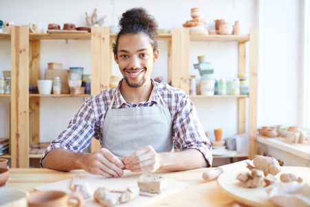 Portrait of young handsome mixed race craftsman sitting at table and shaking hands in workshopの写真素材