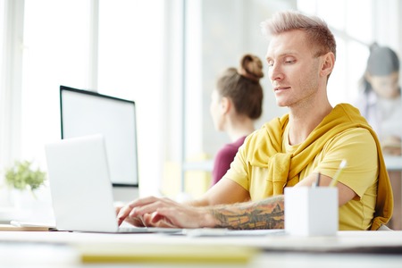 Creative designer typing on laptop while sitting at his workplace at officeの写真素材