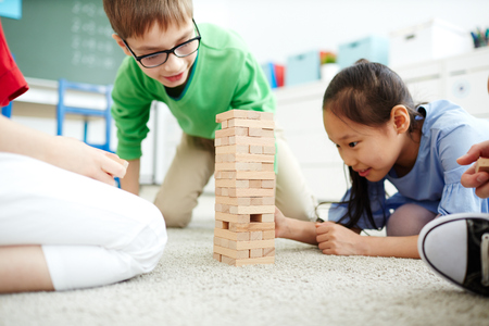 Elementary school kids sitting on the floor and playing with wooden blocksの写真素材