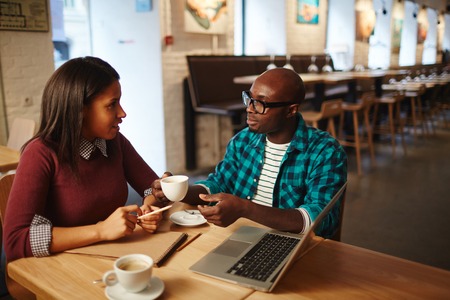 Mixed race woman discussing work with African American male colleague while drinking coffee in cafeの写真素材