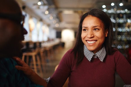 Portrait of young attractive mixed race woman smiling cheerfully while talking to male colleague in cafeの写真素材
