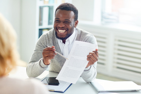 Smiling African American businessman sitting at office desk and discussing details of mutually beneficial cooperation with business partnersの写真素材