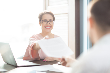 Cheerful woman giving papers to colleagueの写真素材