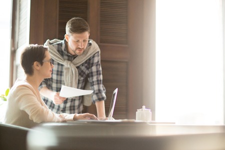 Man with papers helping colleague with laptopの写真素材