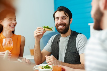 Smiling man holding bread while eating with friendsの写真素材