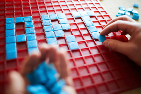 Close up of unrecognizable craftsman laying out  word ART in blue square tiles over red base, copy spaceの写真素材