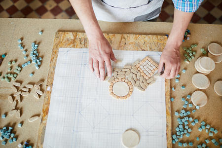 Top view of unrecognizable craftsman laying out shaped marble tiles in pattern while creating mosaic in traditional crafting workshop, copy spaceの写真素材