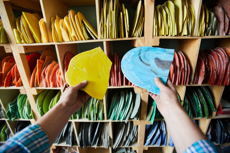 Hands of unrecognizable artisan holding materials and choosing color while standing against tall shelves in workshop, copy spaceの写真素材