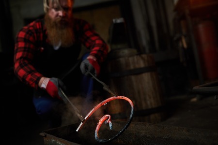 Brutal blacksmith holding metal bar in tongsの写真素材