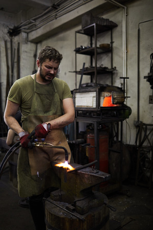 Frowning blacksmith parting metal with cutting torchの写真素材