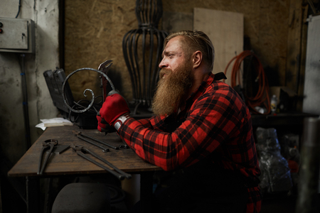 Sad blacksmith checking metal barの写真素材