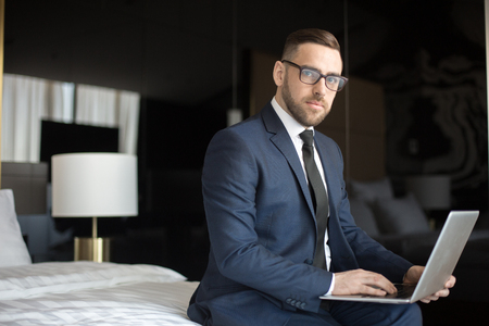 Elegant businessman with laptop on bedの写真素材