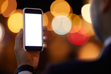 Smartphone with blank touchscreen held by mobile businessman while making outdoor selfieの写真素材