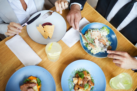 Close-up of unrecognizable business colleagues sitting at table full of food and eating tasty dish at business lunchの写真素材