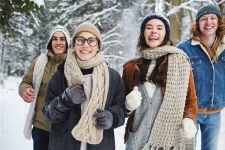 Waist up portrait of four carefree young people running towards camera while having fun in winter forest during vacationの写真素材