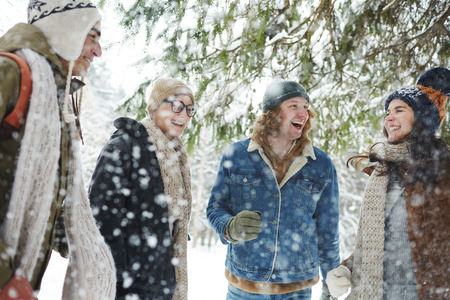 Group of carefree young people having fun in winter forest under snowfall, hiking and resort conceptの写真素材