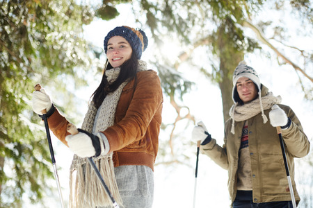 Waist up portrait of happy young couple  skiing in winter forest and looking at camera, focus on woman in frontの写真素材