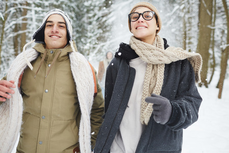 Waist up portrait of happy young couple running towards camera while having fun in winter forest during vacationの写真素材