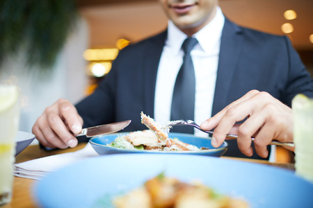 Close-up of businessman on business lunch at restaurant sitting at table eating salad holding fork and knifeの写真素材