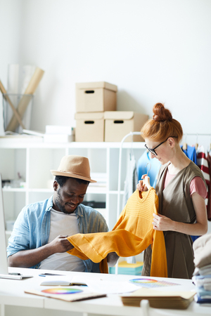 Female designer showing stylish sweater to her colleague and he evaluating the quality of the sweater at atelierの写真素材