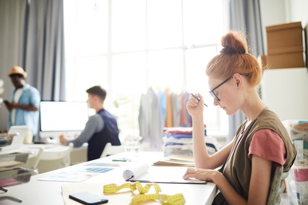 Young tailor sitting at her workplace and concentrated on some document at the workshopの写真素材